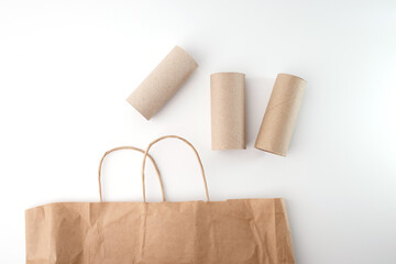 Empty cardboard tubes and brown paper bag on white background. Recycled materials for DIY craft project. Studio shot for design and print. Flat lay composition with copy space.,