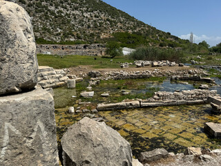 Ruins of an ancient site near a natural spring in a mountainous landscape