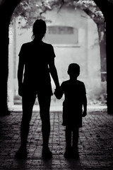 Monochrome silhouette of an adult and child holding hands at the end of a tunnel, with light behind...