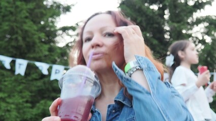 Young beautiful smiling girl. Carefree girl posing on the street taking selfie photo on smartphone. Positively holding and drinking fresh smoothie cocktail in plastic cup with straw. Summer festival