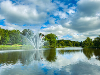 A serene lake with a grand fountain and lush greenery, alongside a captivating sky, offers an ideal...