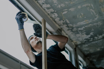 A construction worker is repairing a window frame from the outside.