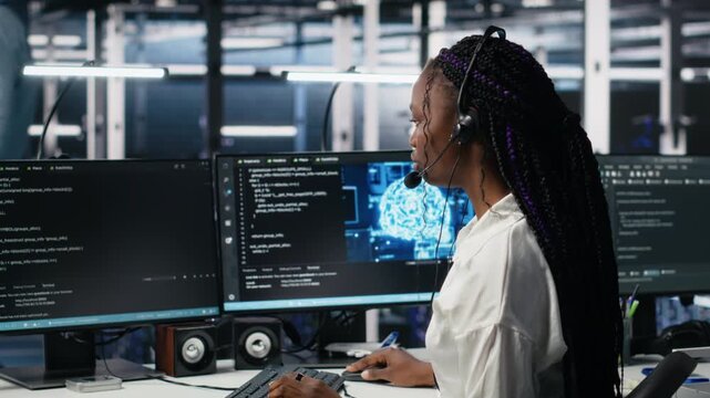 Admin in data center wearing headset assisting users with artificial intelligence troubleshooting. African american woman in server room hub managing support tickets using automated systems, camera A - Powered by Adobe