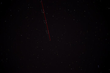 Night sky with red light trail and stars visible in dark sky background