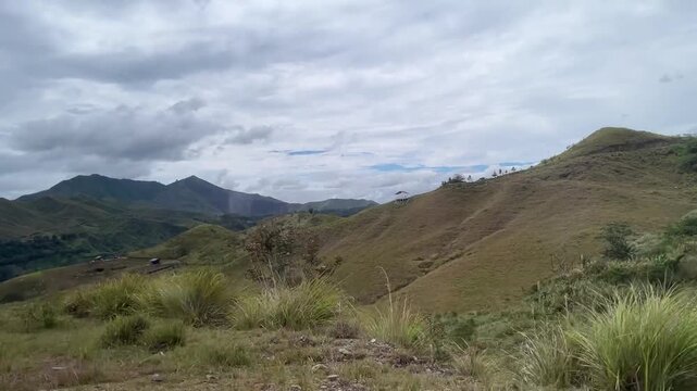 Beautiful landscape featuring rolling green hills and distant mountains, dramatic cloudy sky.