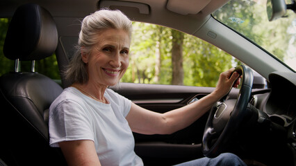 Smiling aged retired Caucasian happy elderly pensioner woman female driver car owner sitting inside...