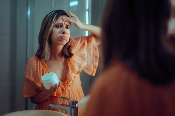Woman Worried About the Effects of Aging Using a Face Cream. Unhappy distressed millennial girl...