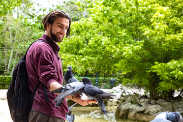 Happy guy feeds and holds a group of pigeons on his arm, enjoying a peaceful connection with birds in an urban park.

