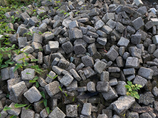 Pile of left over pavers, flooring or concrete block paving, cube shape, with green vines