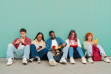Cheerful group of young friends interacting with their mobile devices, sharing moments and laughter while sitting on the ground, showcasing a modern lifestyle of connectivity and friendship.