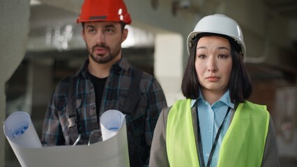 Building business inspection multiethnic builders architects talking blueprint at site Caucasian...