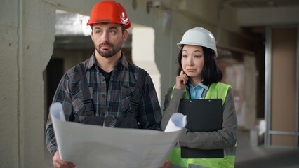 Business multiethnic builders man woman uniform brainstorming talking blueprint site Japanese...