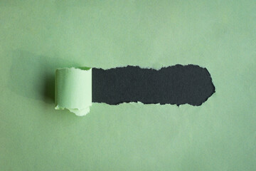 Hole ripped in green paper on black background.