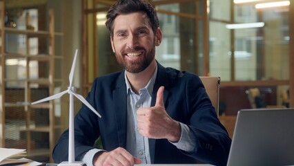 Cheerful Caucasian business man laptop windmill project showing thumb up gesture approval...