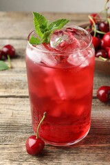 Tasty cherry soda with ice cubes, berries and mint on wooden table, closeup