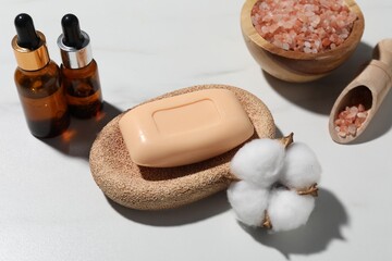 Soap bar, cosmetic products and cotton flower on white marble table, above view