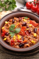 Tasty chili con carne in bowl on wooden table, closeup