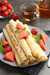 Tasty crepes with strawberries and mint on grey table, closeup
