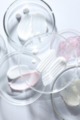 Different cosmetic products in Petri dishes on white background, closeup