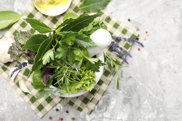 Mortar with pestle, different aromatic herbs and spices on grey table, flat lay. Space for text