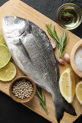 Fresh raw dourade with spices on black table, top view. Fish and seafood delicacies