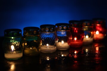 Many grave candles on black table against blue background, closeup