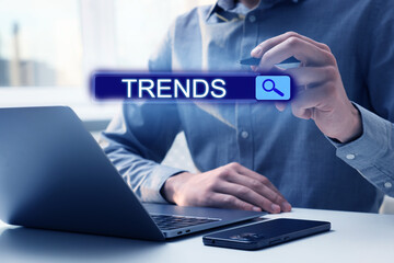 Fototapeta premium Businessman using laptop and virtual screen to find hot tendencies, new ideas, popular directions at table, closeup. Search bar with word Trends