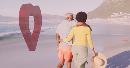 Walking Black couple holding each other on coastal beach, with straw hat and red map pin