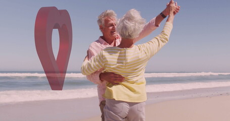 Dancing senior couple raising hands embracing on sandy oceanfront beach, with red heart sculpture