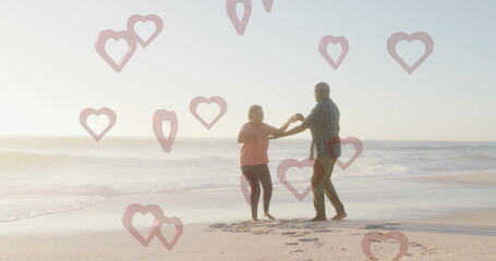 Dancing mature man and senior woman holding hands on shoreline with pink overlays and footprints