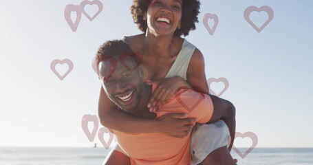 Couple giving piggyback ride and laughing at shoreline in coral tee, green top with heart shapes