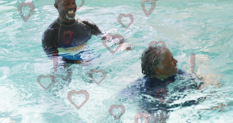 Laughing friends wearing dark swim tops interacting in therapy pool water, with heart-shaped decals