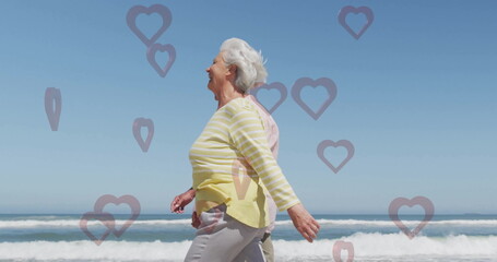 Walking elderly couple in yellow-striped and pink shirts along beach, with heart-shaped graphics