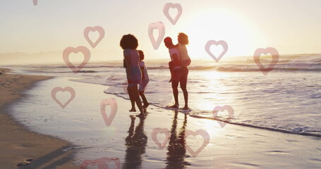 Strolling parents carrying children along wet sand at beach sunset, with heart overlays, copy space