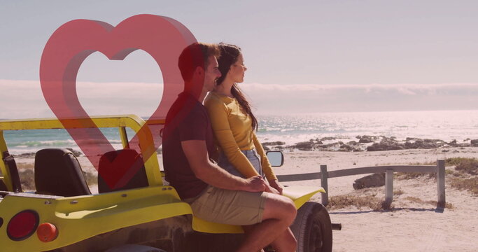 Sitting couple on yellow dune buggy facing sea horizon at sandy shore, with wooden guardrail