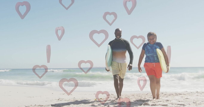 Walking mature man and senior woman surfers carrying surfboards on sandy beach near ocean waves - Powered by Adobe