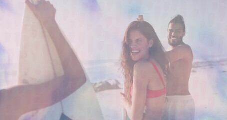 Laughing friends wearing swimwear holding three surfboards upright at sandy shore, with ocean waves