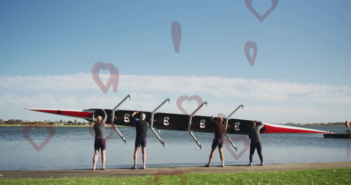 Four rowers wearing sports attire lifting racing shell on shoreline by dock, with riggers and oars - Powered by Adobe