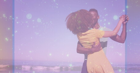 Dancing couple wearing yellow dress and short sleeved shirt spinning at beach shore, pastel filter