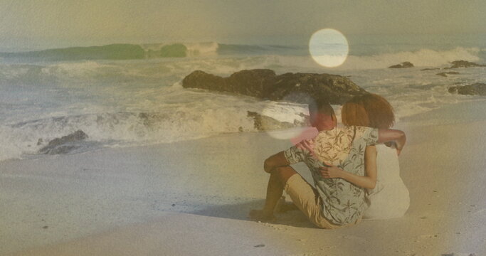 Sitting couple gazing toward ocean waves on sandy shoreline, with rocky outcrops and shells