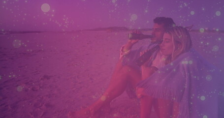Sitting couple sipping drinks on sandy beach, with fringed shawl and dark bottles, copy space