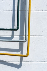 Asymmetrical yellow, gray and green pipes on a white brick wall