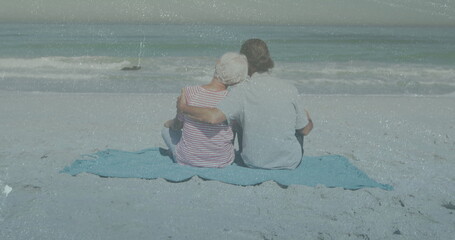 Sitting mother and son watching calm sea at sandy beach, with light blue blanket