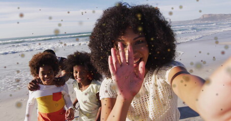 Taking selfie woman with curly hair wearing white top capturing family at beach, with smartphone