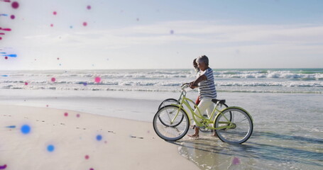 Walking mature couple pushing cruiser bicycles along ocean shoreline with gentle waves, copy space
