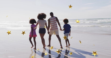 Strolling family of four along wet shoreline at low tide on beach, with golden star overlays