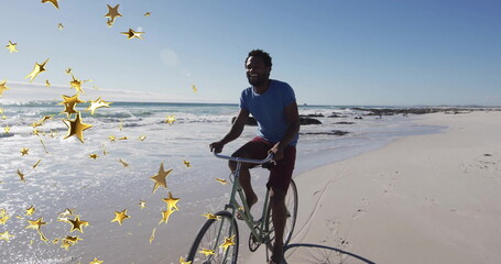 Riding man in blue shirt, maroon shorts pedaling wet sand at beach, green bicycle, golden stars