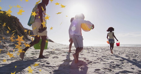 Walking family group carrying striped beach bag and inflatable ball on sandy shore, holding buckets