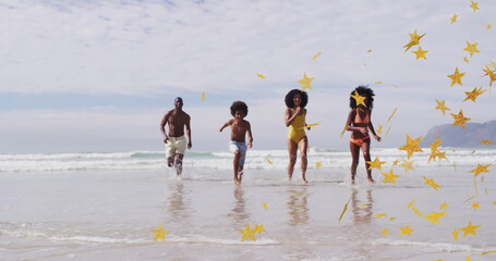 Running family of four in swimwear splashing along shallow surf, with gold star-shaped confetti