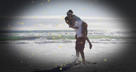 Carrying woman piggyback, man in striped t-shirt striding through surf on beach, with golden light